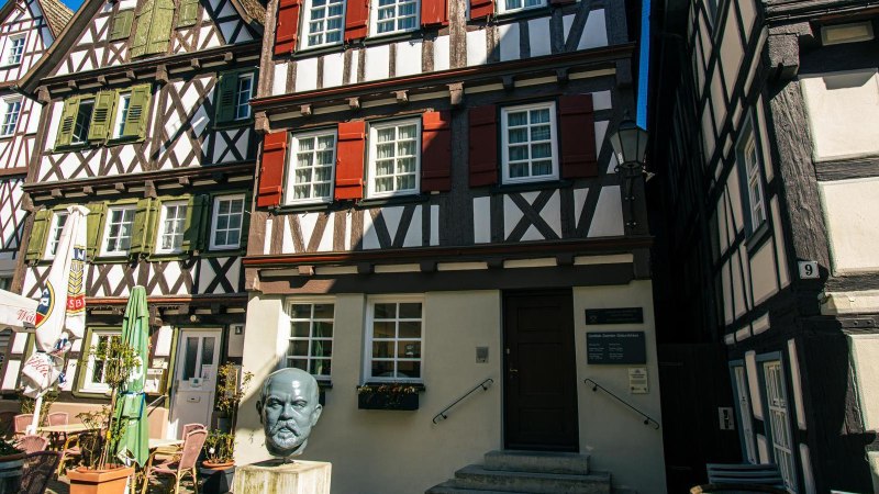 Half-timbered houses in Schorndorf with a bust of Gottlieb Daimler in the foreground. Parasols and a caf&eacute; area can also be seen., &copy; Stuttgart-Marketing GmbH, Sarah Schmid