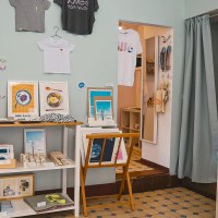 Ein Atelier mit Kunstwerken, T-Shirts an der Wand, bunten Karten und Dekorationen. Regale zeigen verschiedene kreative Produkte., &copy; Vogelsangatelier, Stuttgart