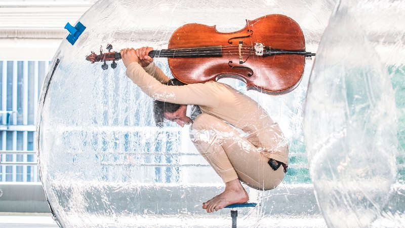 Eine Person sitzt in einer durchsichtigen Kugel und hält ein Cello. Die Szene wirkt künstlerisch und ungewöhnlich., © FREDERIK LAUX PHOTOGRAPHY Eine Person sitzt in einer durchsichtigen Kugel und hält ein Cello. Die Szene wirkt künstlerisch und ungewöhnlich., © FREDERIK LAUX PHOTOGRAPHY