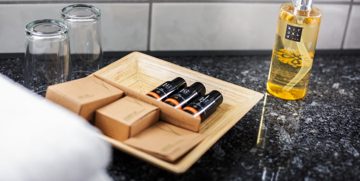 Hotel-Badezimmer mit Pflegeprodukten auf einem Tablett, zwei Gläsern und einem Rituals Infinity Seifenspender auf einer Granitoberfläche., © Kronen Hotel GmbH Hotel-Badezimmer mit Pflegeprodukten auf einem Tablett, zwei Gläsern und einem Rituals Infinity Seifenspender auf einer Granitoberfläche., © Kronen Hotel GmbH