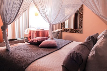 Ein elegantes Hotelzimmer mit Himmelbett, dekorativen Kissen und einem Tisch mit Stühlen. Ein großer Spiegel hängt an der Wand., © Hotel Princess Ein elegantes Hotelzimmer mit Himmelbett, dekorativen Kissen und einem Tisch mit Stühlen. Ein großer Spiegel hängt an der Wand., © Hotel Princess