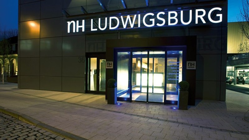 Eingang des NH Hotels in Ludwigsburg bei Nacht, beleuchtet mit blauem Licht. Der Schriftzug 'NH LUDWIGSBURG' ist gut sichtbar., &copy; NH Ludwigsburg