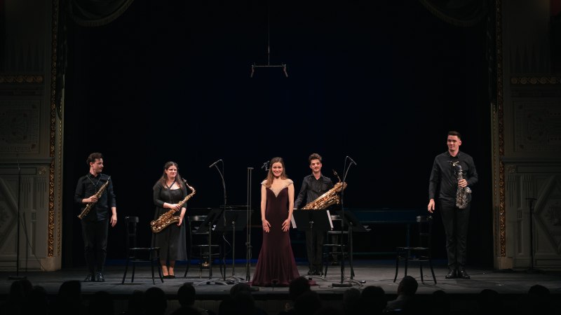 Ein Saxophonquartett und eine S&auml;ngerin verbeugen sich auf einer B&uuml;hne vor dem Publikum. Die Musiker halten ihre Instrumente in den H&auml;nden., &copy; Luca Cs&ouml;rge&ouml;