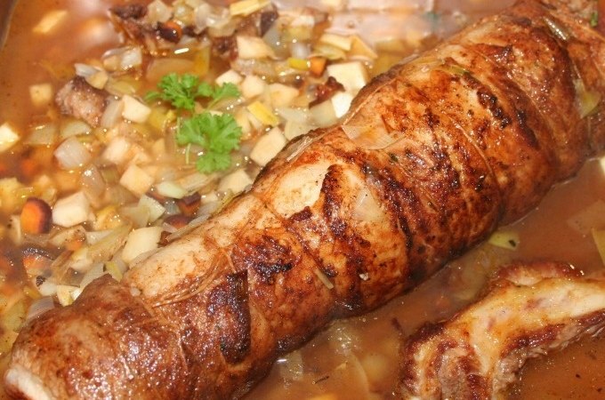 A rolled roast in a pan, surrounded by diced vegetables and a brown sauce, garnished with a sprig of parsley., &copy; Kultweine-Kochwelten-Kunst&uuml;cke - Kochschule Sonja Lenz