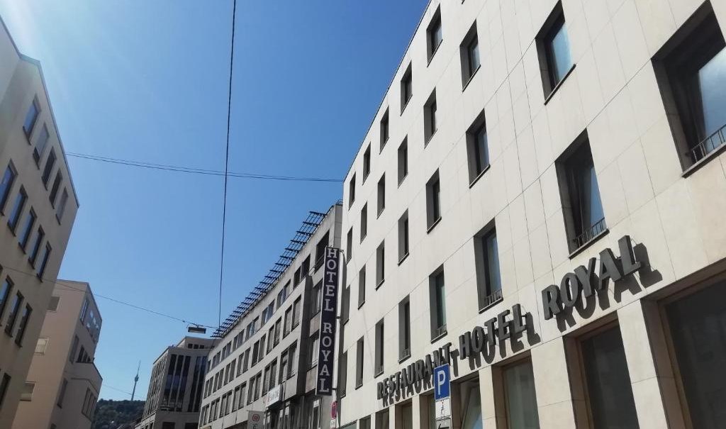 Ein modernes Gebäude mit dem Schriftzug 'Hotel Royal' unter blauem Himmel. Die Straße ist von weiteren Gebäuden gesäumt., © Hotel Royal
