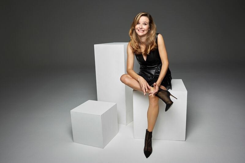 Eine Frau in einem schwarzen Kleid sitzt lächelnd auf weißen Würfeln in einem Fotostudio. Der Hintergrund ist neutral grau gehalten., © Theaterhaus Stuttgart e.V. Eine Frau in einem schwarzen Kleid sitzt lächelnd auf weißen Würfeln in einem Fotostudio. Der Hintergrund ist neutral grau gehalten., © Theaterhaus Stuttgart e.V.