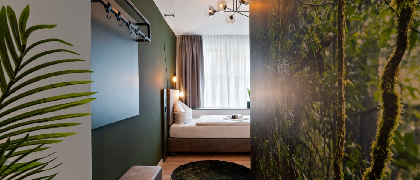 Modernes Einzelzimmer mit gr&uuml;nem Thema, Pflanzenmotiv an der Wand, stilvoller Beleuchtung und gem&uuml;tlichem Bett., &copy; JUNGLE N&deg;5 GmbH