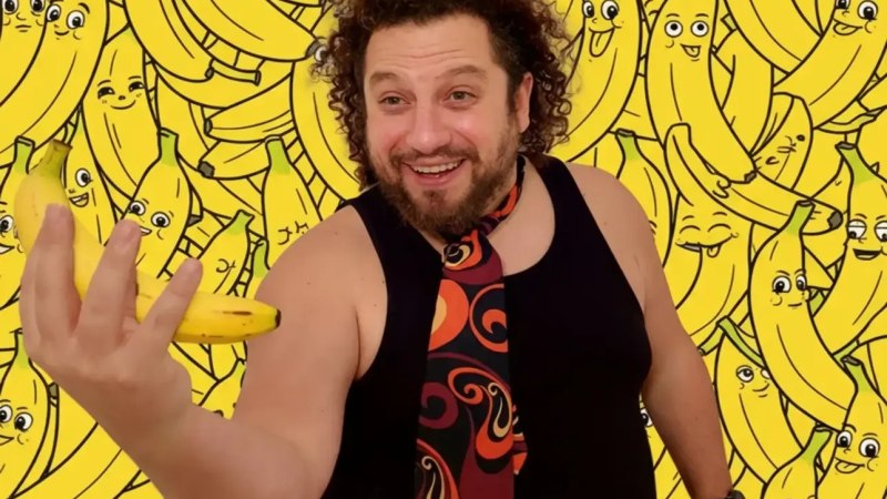 Ein Mann mit lockigem Haar hält eine Banane in der Hand. Im Hintergrund sind viele gezeichnete Bananen mit Gesichtern zu sehen., © Theater am Olgaeck Ein Mann mit lockigem Haar hält eine Banane in der Hand. Im Hintergrund sind viele gezeichnete Bananen mit Gesichtern zu sehen., © Theater am Olgaeck