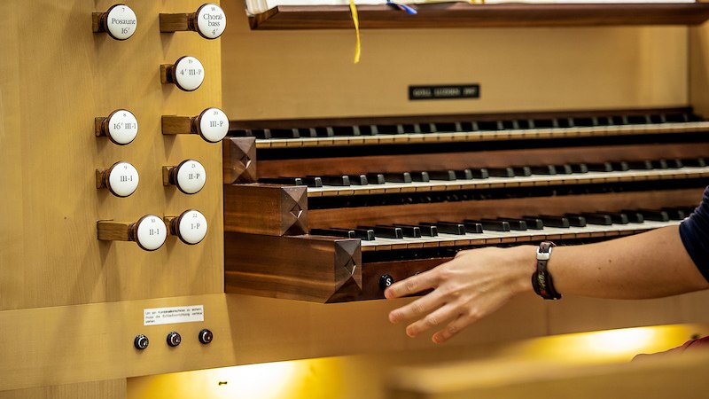 Eine Hand bedient die Register einer Orgelkonsole. Die Tasten und Register sind gut sichtbar, im Hintergrund liegen Noten., &copy; Staatliche Hochschule f&uuml;r Musik und Darstellende Kunst