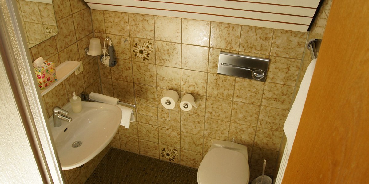 Kleines Badezimmer mit Waschbecken, Toilette, Handtuchhalter und Fliesen mit Blumenmuster. Ein Fön hängt an der Wand., © Hotelmärchen Kleines Badezimmer mit Waschbecken, Toilette, Handtuchhalter und Fliesen mit Blumenmuster. Ein Fön hängt an der Wand., © Hotelmärchen