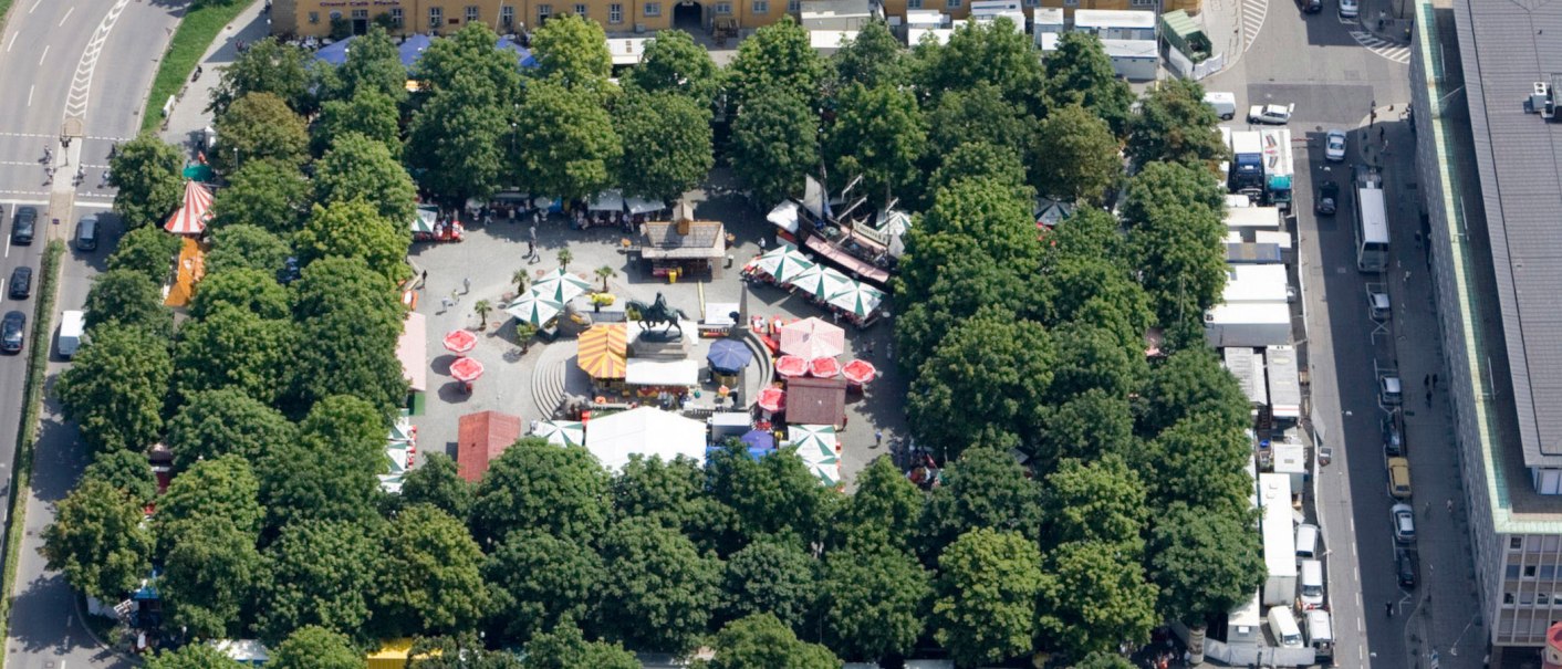 Aerial view of Karlsplatz in Stuttgart. Market stalls and colorful umbrellas are surrounded by trees. An equestrian statue stands in the center., &copy; Stuttgart-Marketing GmbH