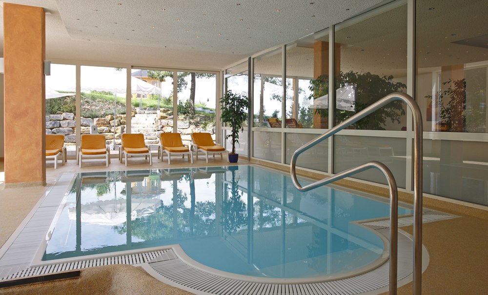Moderner Wellnessbereich mit Pool, Liegestühlen und großen Fenstern mit Blick ins Grüne. Entspannte Atmosphäre im Badhotel Stauferland., © Badhotel Stauferland