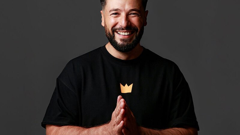 A man with a beard and white T-shirt smiles at the camera. The background is gray and simple., &copy; Theaterhaus Stuttgart e.V.