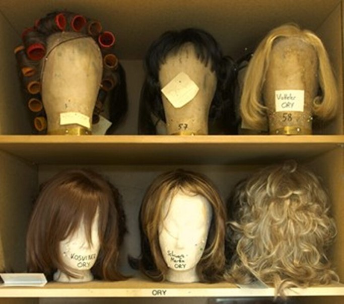 Regal mit sechs Per&uuml;cken auf Styropork&ouml;pfen, einige mit Lockenwicklern. Beschriftungen auf den K&ouml;pfen sind sichtbar., &copy; W&uuml;rttembergische Staatstheater Stuttgart
