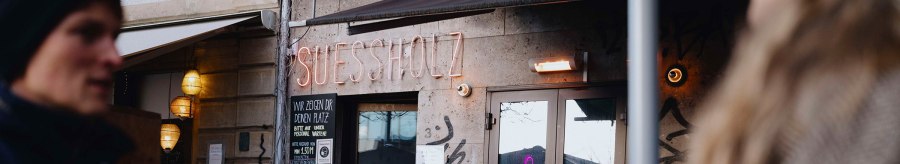 Exterior view of the 'Suessholz' caf&eacute; in the Leonhardsviertel. People are sitting outside, chatting. Graffiti on the walls, neon light in the window., &copy; &copy; Stuttgart-Marketing GmbH, Alwin Maigler