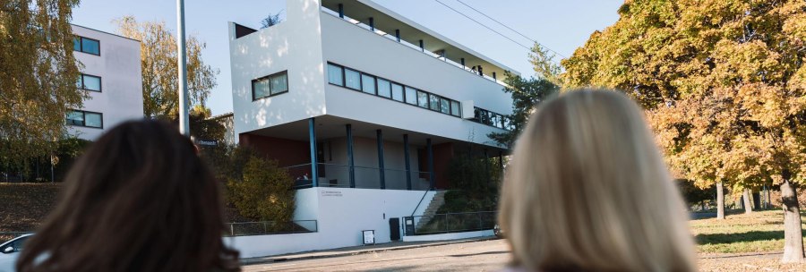 Two people look at the Le Corbusier house in the Weißenhofsiedlung. Modern building with clear lines, surrounded by autumnal trees., © Stuttgart-Marketing GmbH, wpsteinheisser