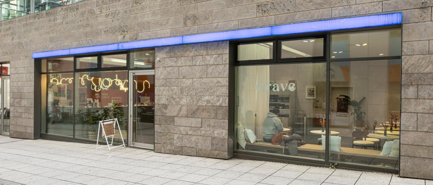 Große Fensterfronten, die Blick auf das Café im Inneren freigeben: Holztische, weiße Kissen., © Stuttgart-Marketing GmbH, Sarah Schmid Große Fensterfronten, die Blick auf das Café im Inneren freigeben: Holztische, weiße Kissen., © Stuttgart-Marketing GmbH, Sarah Schmid