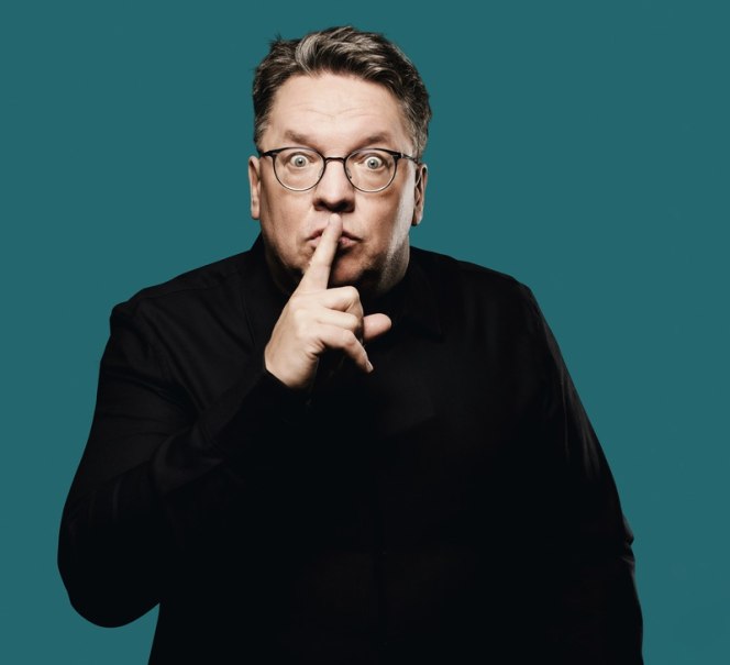 Person mit Brille und schwarzem Hemd hält den Finger vor den Mund, als Zeichen zum Schweigen, vor einem blauen Hintergrund., © Renitenztheater Stuttgart e.V. Person mit Brille und schwarzem Hemd hält den Finger vor den Mund, als Zeichen zum Schweigen, vor einem blauen Hintergrund., © Renitenztheater Stuttgart e.V.