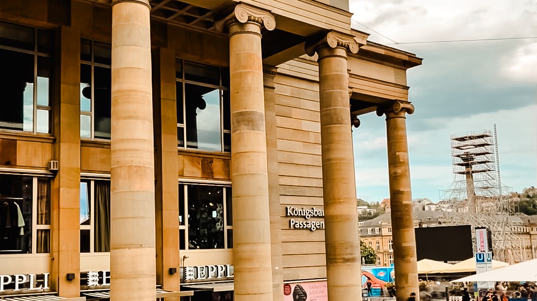 Eingang der Königsbau Passagen mit imposanten Säulen. Menschen bewegen sich auf dem Platz davor. Im Hintergrund ist eine Baustelle sichtbar., © Königsbau Eingang der Königsbau Passagen mit imposanten Säulen. Menschen bewegen sich auf dem Platz davor. Im Hintergrund ist eine Baustelle sichtbar., © Königsbau