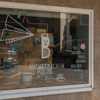 Schaufenster des Buchladens 'Buchst&auml;bchen' in Stuttgart. Dekoriert mit B&uuml;chern und einem Papierflieger. Passanten betrachten das Schaufenster., &copy; SMG, Sarah Schmid