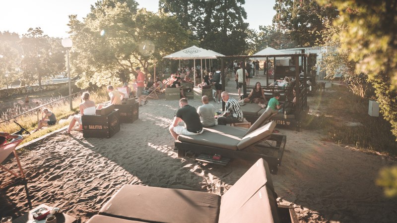Menschen entspannen an einem sonnigen Stadtstrand in Stuttgart. Liegest&uuml;hle und Sonnenschirme bieten eine gem&uuml;tliche Atmosph&auml;re im Sand., &copy; Classic Rock Caf&eacute; Gastronomie- Betriebs GmbH
