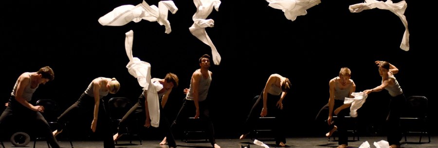 Dancers on a dark stage throw white scarves into the air. They wear black clothes and move in sync., &copy; Regina Brocke