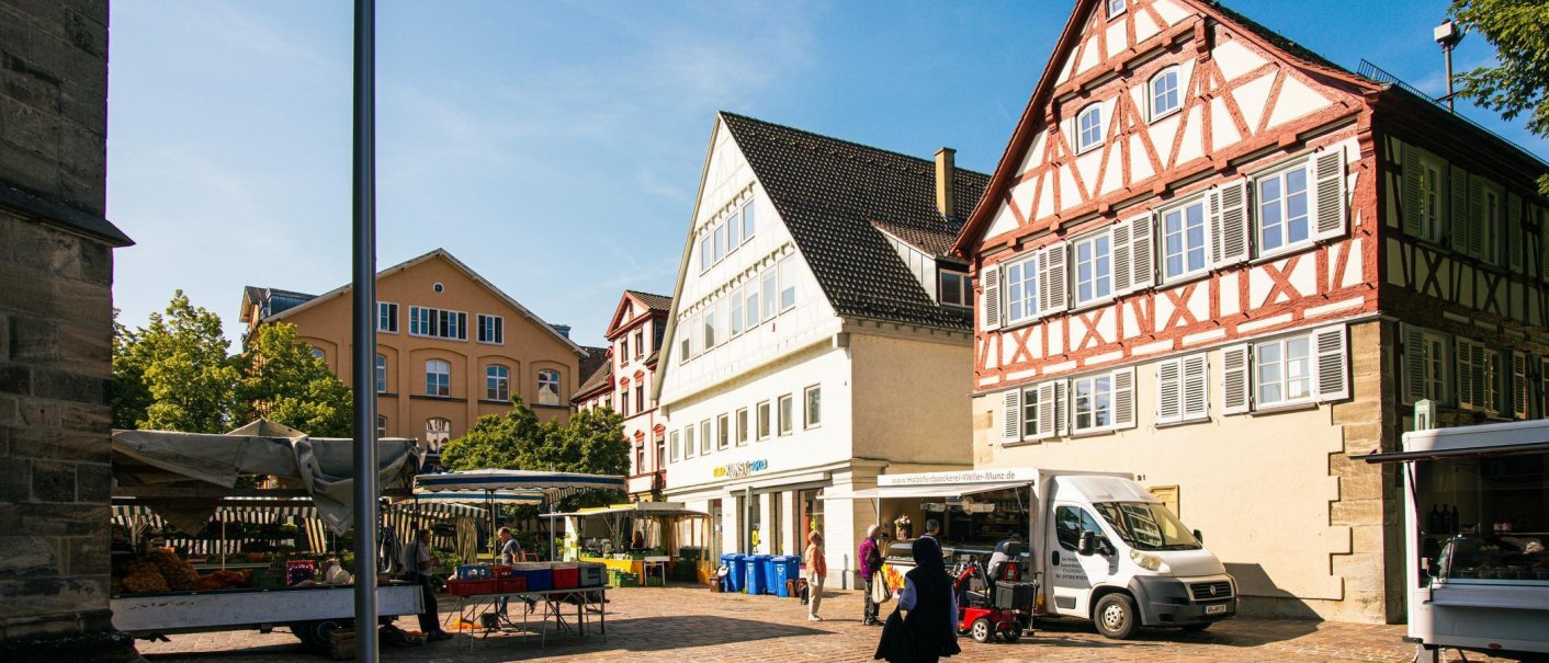 A sunny market square in Schwäbisch Gmünd with historic half-timbered houses and market stalls. People stroll through the old town., © Stuttgart-Marketing GmbH, Sarah Schmid