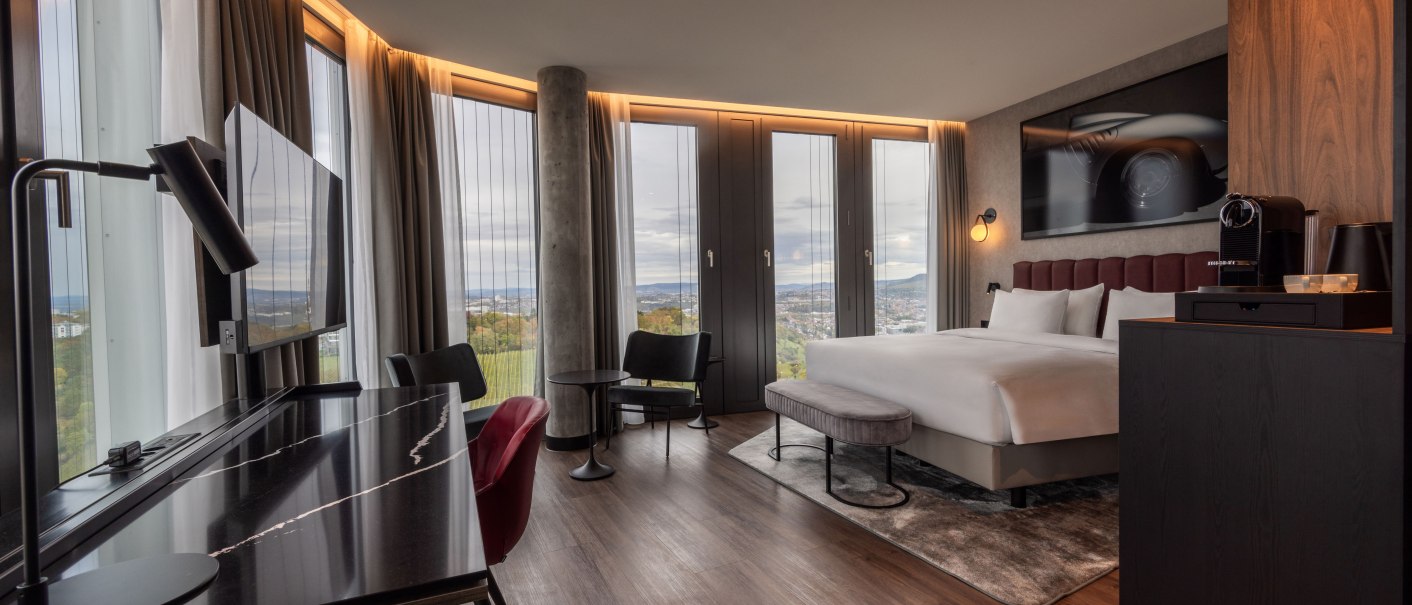 Modernes Eckzimmer mit Panoramafenstern, Doppelbett, Schreibtisch, Sessel und Kaffeemaschine. Elegantes Design mit Holzboden und stilvoller Beleuchtung., &copy; Radisson Hotel Group