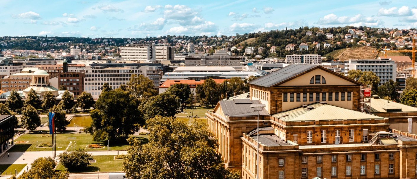 Panoramablick auf eine Stadt mit historischen Gebäuden, grünen Parks und Hügeln im Hintergrund unter einem blauen Himmel mit Wolken., © Stuttgart-Marketing GmbH, Sarah Schmid
