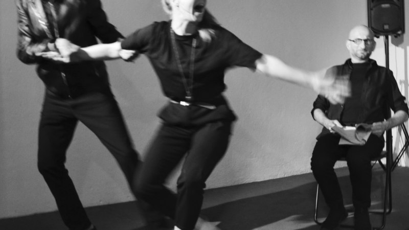 Schwarz-weiß-Foto: Eine Frau wird von einem Mann gezogen, während ein anderer Mann sitzt und zuschaut. Die Szene wirkt dynamisch und emotional., © Theater 360 Grad