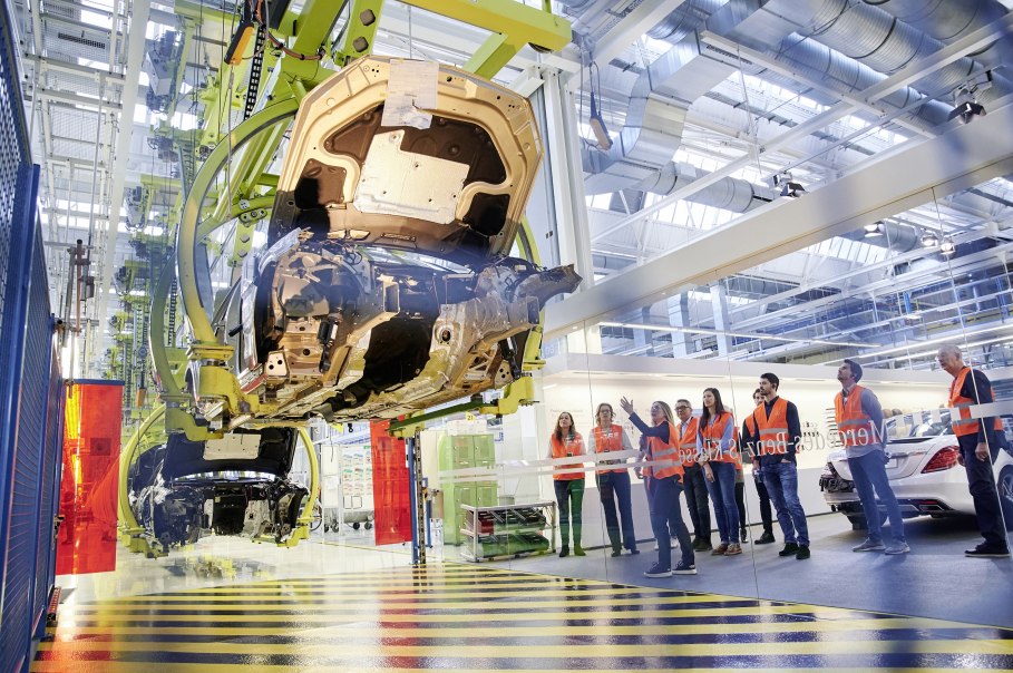 Besucher in orangefarbenen Westen beobachten die Fahrzeugmontage in einer Mercedes-Benz Produktionshalle in Sindelfingen., © Mercedes-Benz AG Besucher in orangefarbenen Westen beobachten die Fahrzeugmontage in einer Mercedes-Benz Produktionshalle in Sindelfingen., © Mercedes-Benz AG