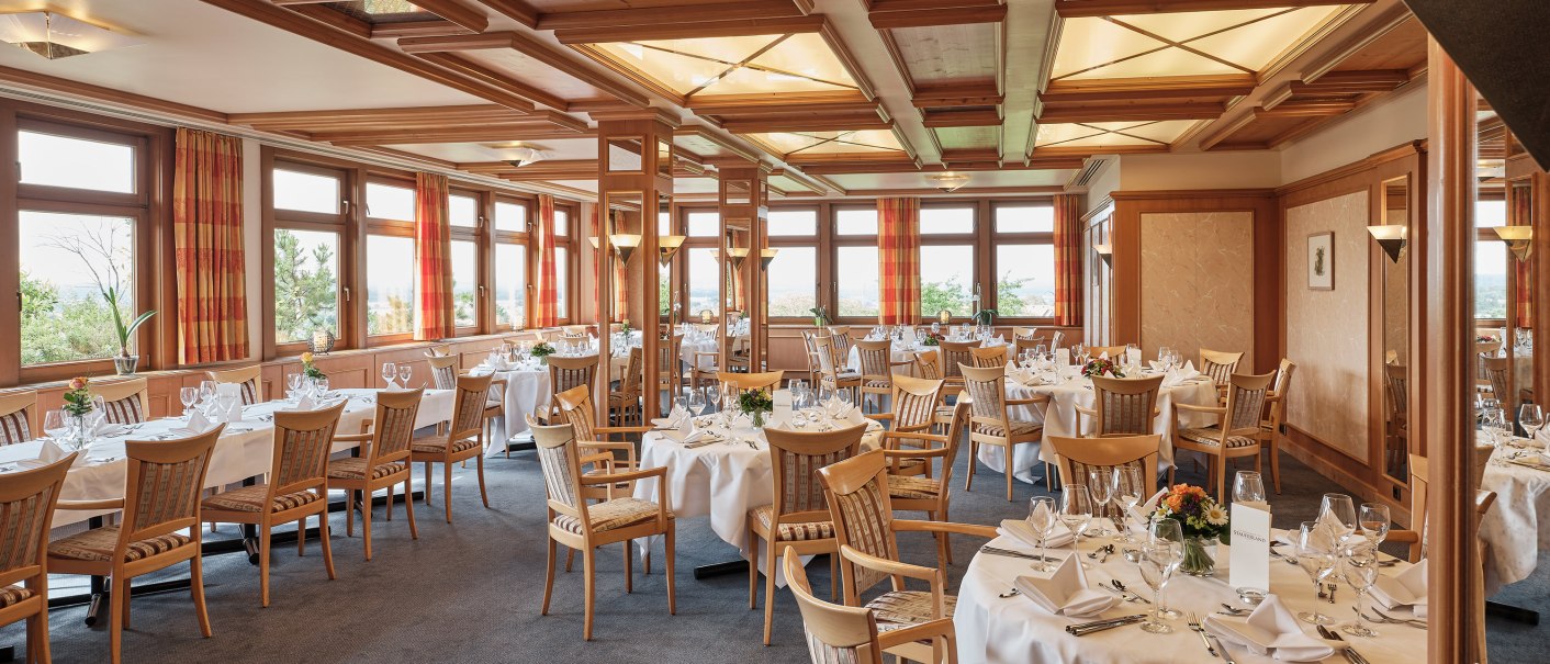Eleganter Speisesaal mit gedeckten Tischen, Holzdekor und großen Fenstern. Die Tische sind mit weißen Tischdecken und Geschirr eingedeckt., © Badhotel Restaurant Stauferland
