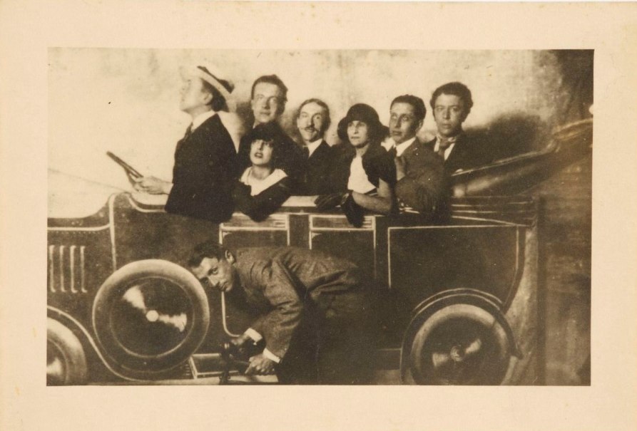 Eine Gruppe von Menschen posiert in einem gemalten Auto auf einem Jahrmarkt. Die Szene wirkt humorvoll und inszeniert., &copy; Anonym, Jahrmarkt auf dem Montmartre, 1923, Staatsgalerie Stuttgart, Graphische Sammlung, erworben 2025 aus Mitteln der Museumsstiftung Baden-W&uuml;rttemberg, Sammlung Dietmar Siegert