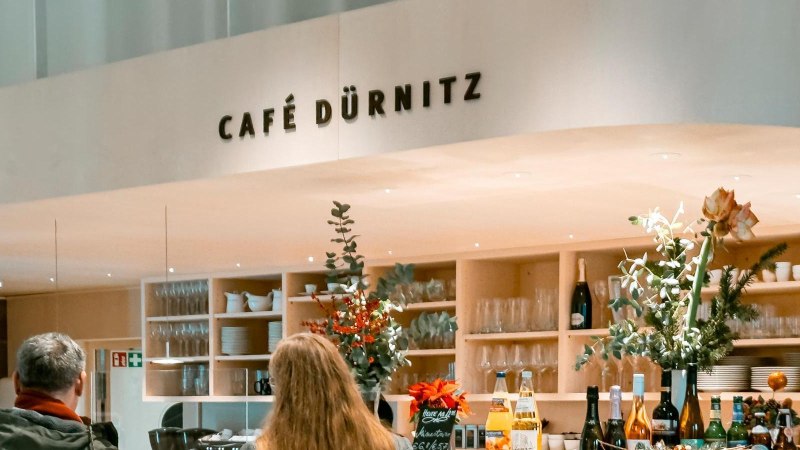 Theke mit Getr&auml;nken und Kuchenvitrine, dekoriert mit Pflanzen. Drei Personen stehen an., &copy; SMG, Sarah Schmid