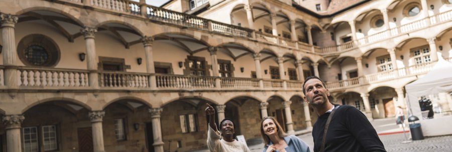 Three people stand in the inner courtyard of the Württemberg State Museum and look upwards. The inner courtyard is surrounded by arcades and historic buildings., © Stuttgart-Marketing GmbH, wpsteinheisser