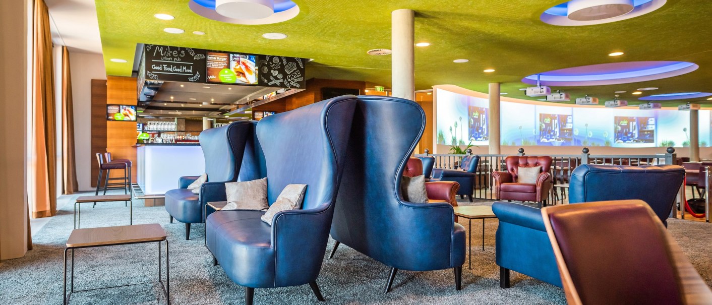 Modern hotel bar with blue armchairs, green ceiling and illuminated counter. Cozy atmosphere with stylish furniture and decoration., © Hilton Garden Inn Stuttgart Neckarpark Modern hotel bar with blue armchairs, green ceiling and illuminated counter. Cozy atmosphere with stylish furniture and decoration., © Hilton Garden Inn Stuttgart Neckarpark