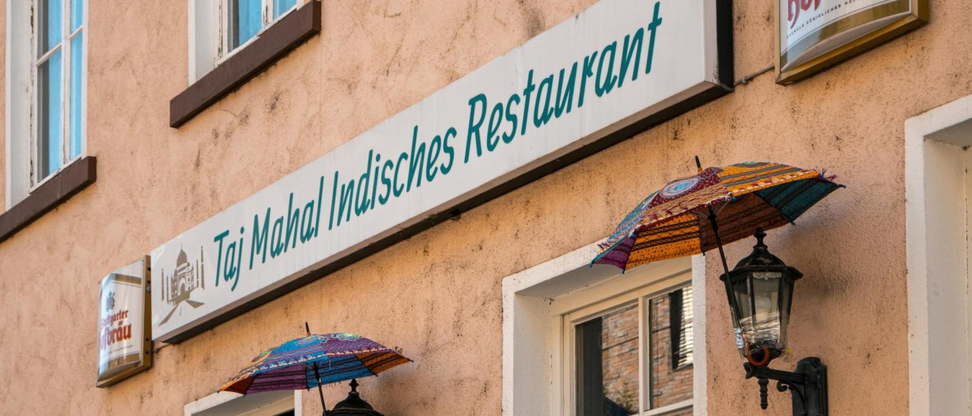 Fassade eines indischen Restaurants in Stuttgart mit bunten Schirmen und einem Schild mit der Aufschrift 'Taj Mahal Indisches Restaurant'., © SMG, Sarah Schmid Fassade eines indischen Restaurants in Stuttgart mit bunten Schirmen und einem Schild mit der Aufschrift 'Taj Mahal Indisches Restaurant'., © SMG, Sarah Schmid