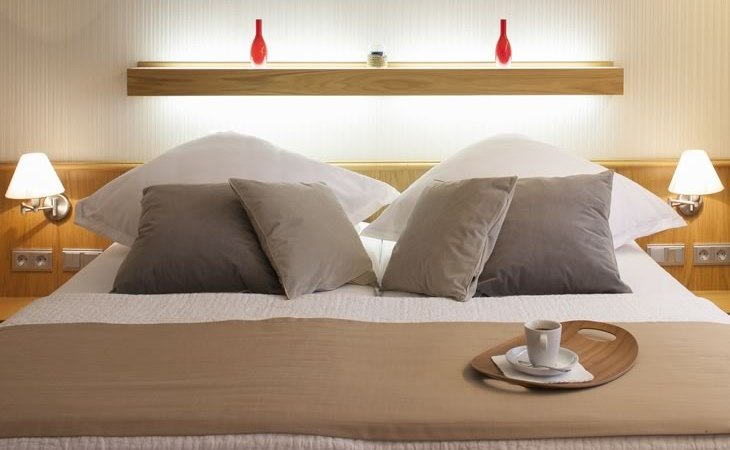 Modernes Schlafzimmer mit Doppelbett, dekoriert mit Kissen und Tablett mit Tasse. Zwei rote Vasen auf einem Regal im Hintergrund., © Hotel Drei Morgen Modernes Schlafzimmer mit Doppelbett, dekoriert mit Kissen und Tablett mit Tasse. Zwei rote Vasen auf einem Regal im Hintergrund., © Hotel Drei Morgen